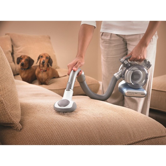 BLACK+DECKER PD1420LP handheld vacuum cleaning beige sofa with two dogs in background.