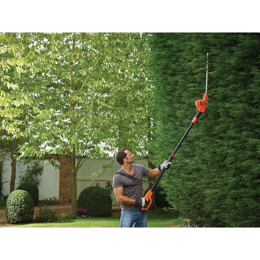 BLACKDECKER PH5551 pole hedge trimmer used by a person trimming tall green hedge in garden.