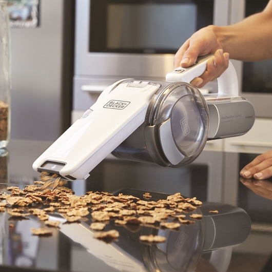 BLACK+DECKER PV1820L handheld vacuum cleaning cereal from black countertop, side view.