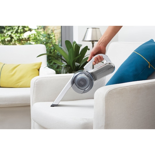 BLACKDECKER PV1820L handheld vacuum cleaner in use on a white armchair, cleaning upholstery.