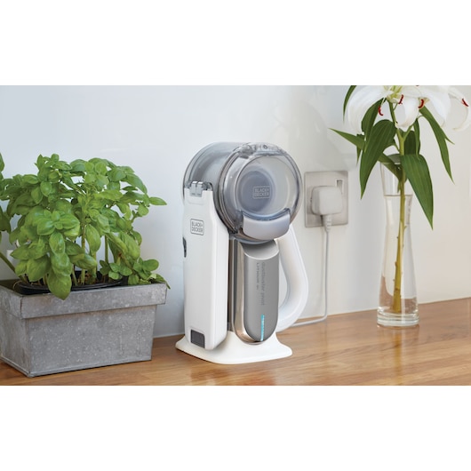 BLACKDECKER PV1820L handheld vacuum cleaner on charging base, placed on kitchen counter near potted plant and flower vase.
