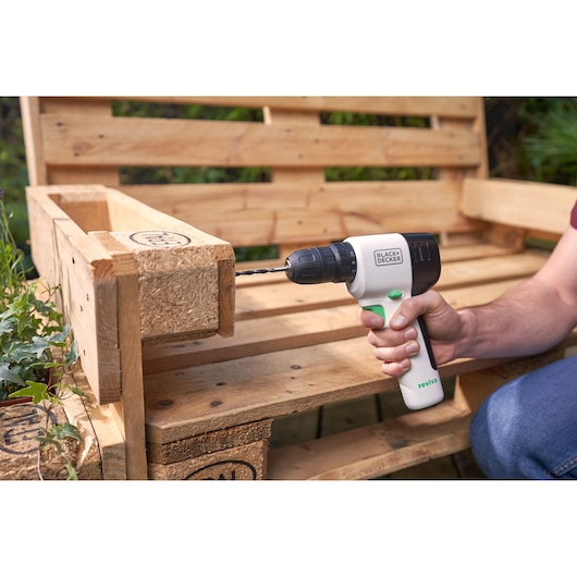 BLACKDECKER REVDD12C cordless drill in use on wooden pallet bench outdoors.