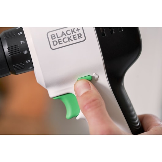 Close-up photo of BLACK+DECKER REVDD12C power drill handle with hand pressing green switch.