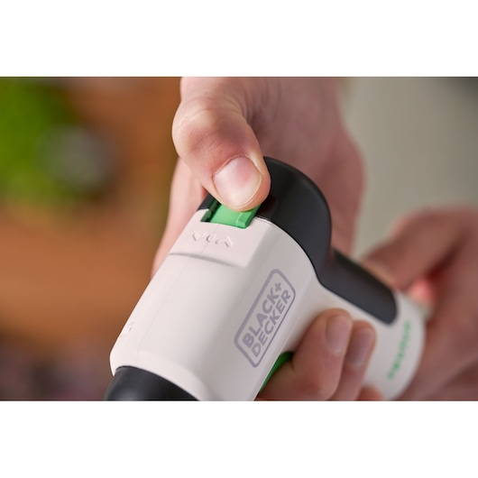 Photo of BLACK+DECKER REVSD4C screwdriver close-up, hand pressing green switch on white and black tool.