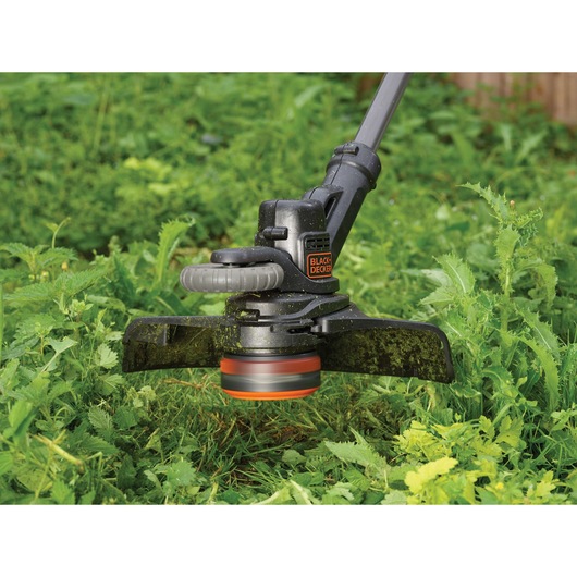 BLACK+DECKER STC1820PCB grass trimmer in use, trimming green weeds and grass in a garden.
