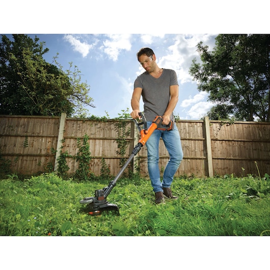 Photo of BLACKDECKER STC1820PCB grass trimmer being used in a garden.