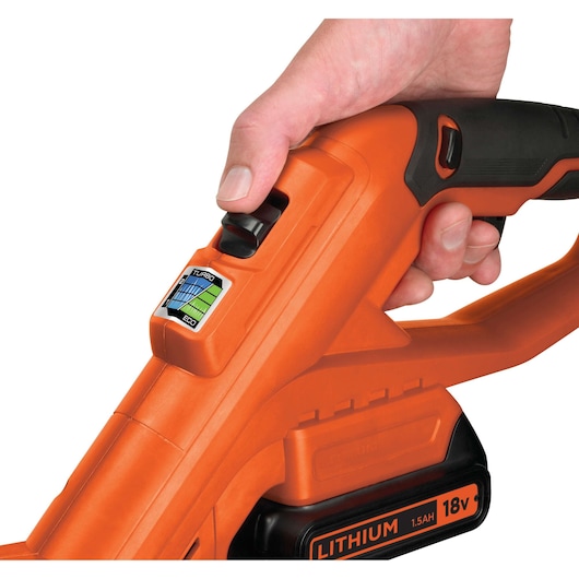 Close-up of a hand operating the power switch on an orange BLACK+DECKER cordless tool with an 18V 1.5Ah lithium battery.