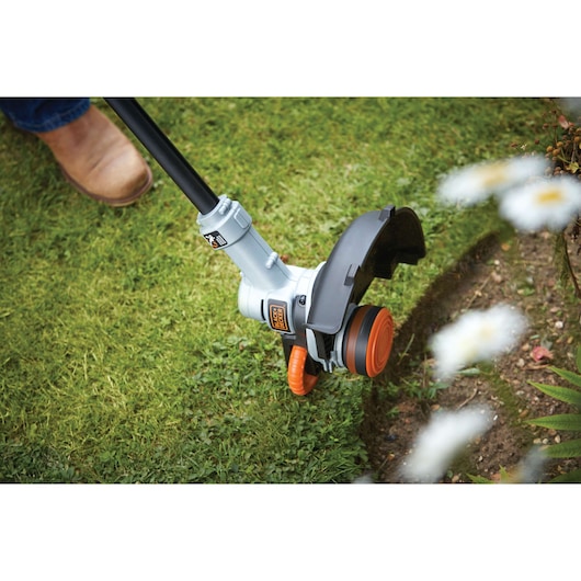 A BLACK+DECKER grass trimmer being used to edge a lawn along a flower bed.